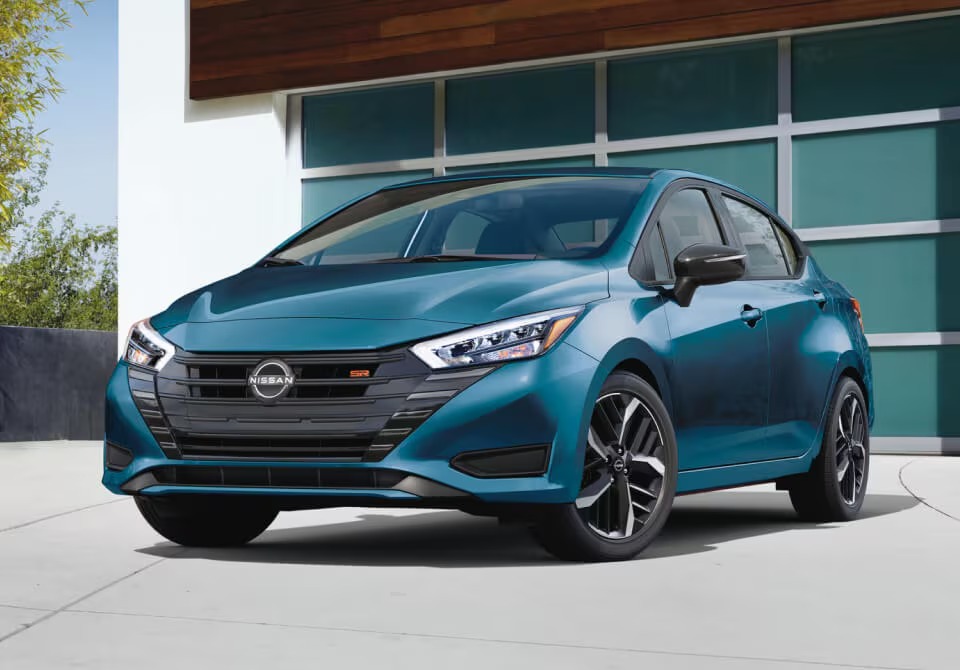 Nissan Versa bleue stationnée devant une maison pour illustrer une citadine usagée abordable et économique en essence.