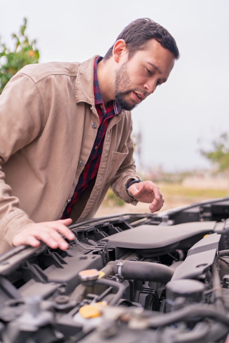 Conducteur inspectant le compartiment moteur d’un véhicule en panne, illustrant les signes possibles d’un alternateur défectueux.