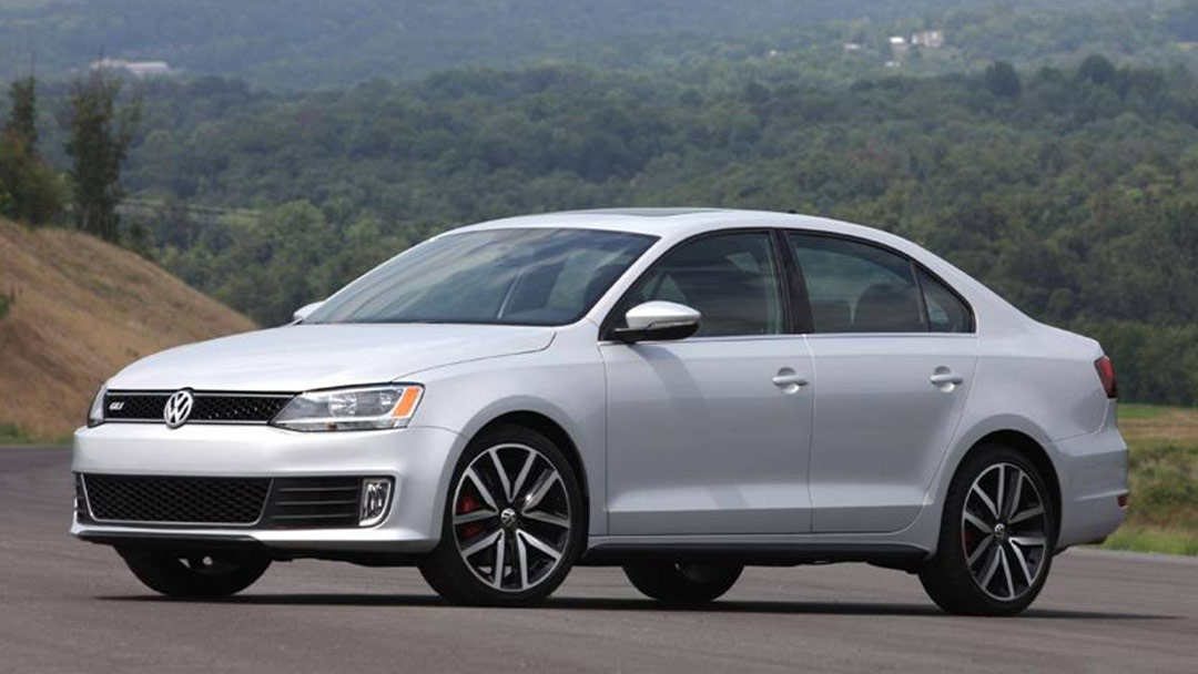 Vue  3/4 avant et latérale de la Volkswagen Jetta sur route de campagne avec vue sur forêt