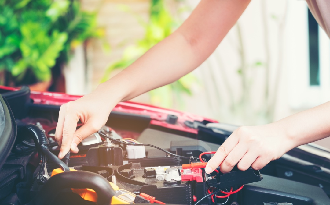 Manipulation des bornes et des câbles d’une batterie automobile sous le capot, illustrant l’entretien et les bonnes pratiques pour prolonger sa durée de vie.