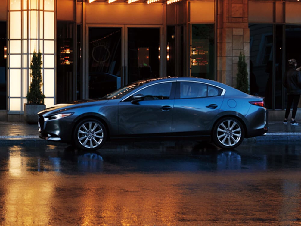 Mazda3 grise sous la pluie en ville pour représenter une citadine usagée sportive et efficace.