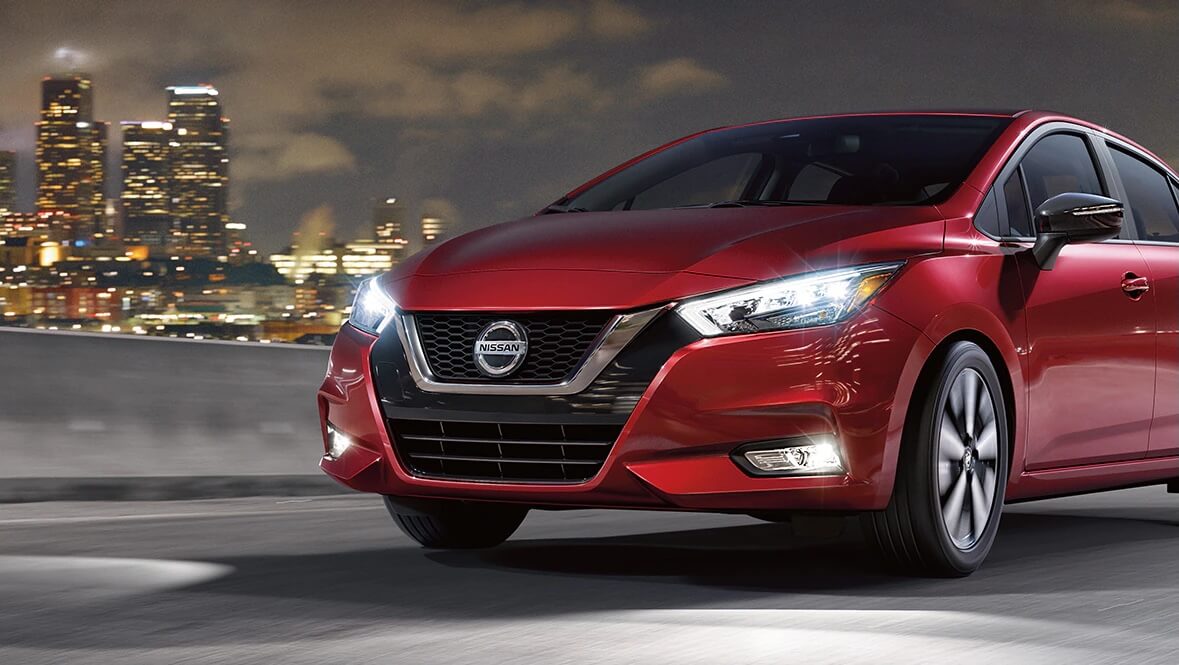 Nissan Versa 2021 rouge vue de trois quarts avant en conduite de nuit en milieu urbain, berline sous-compacte reconnue pour sa faible consommation et son prix abordable au Québec.
