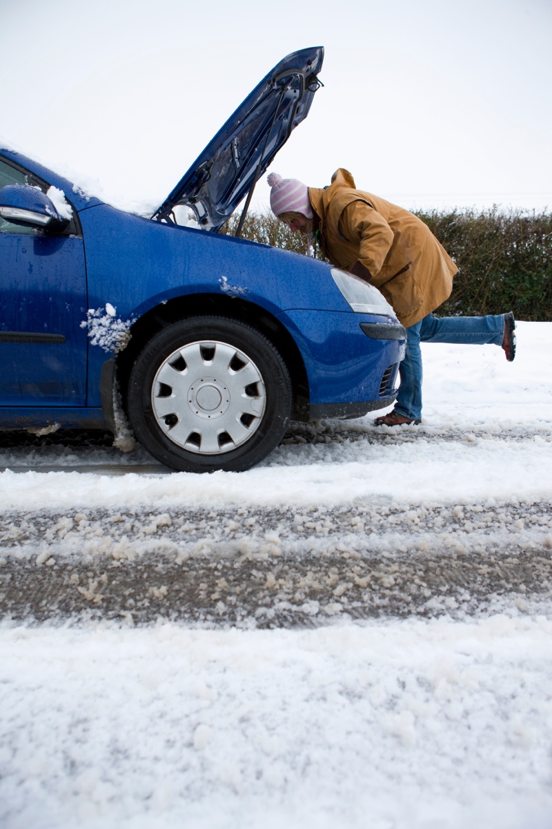 Conducteur tentant de démarrer une voiture en hiver avec le capot ouvert, illustrant l’impact du froid québécois sur la durée de vie d’une batterie d’auto.