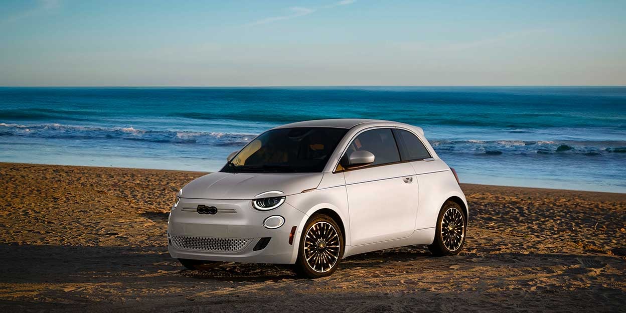 Fiat 500e blanche sur la plage pour illustrer une petite voiture électrique pas chère et économique.