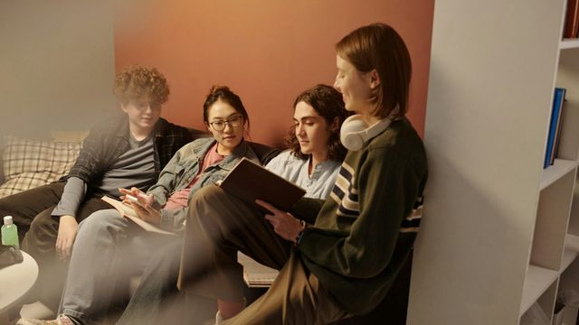 Groupe d'étudiants étudiant ensemble assis sur le canapé et faisant des devoirs dans un salon d'université confortable avec une faible lumière