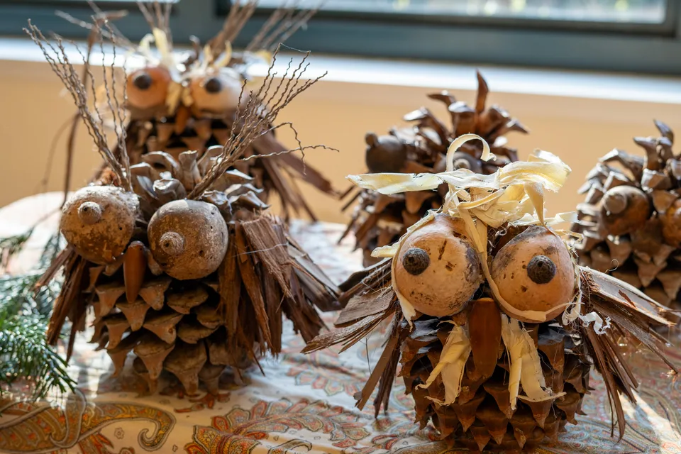 Handmade decorative owl figurines crafted from pinecones, bark, and acorns on a patterned tablecloth