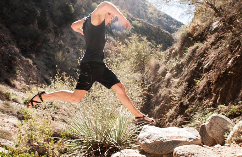 A man jumping on rocks wearing middle bear winged barefoot sandals