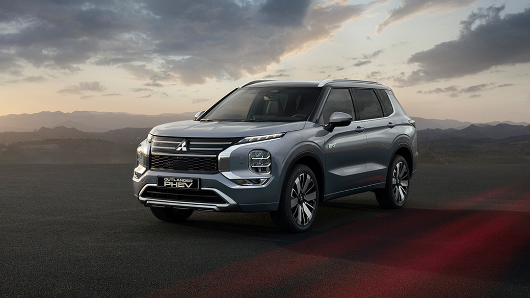 Vue 3/4 avant et latérale du Mitsubishi Outlander PHEV 2025 en arrêt sur route de sable