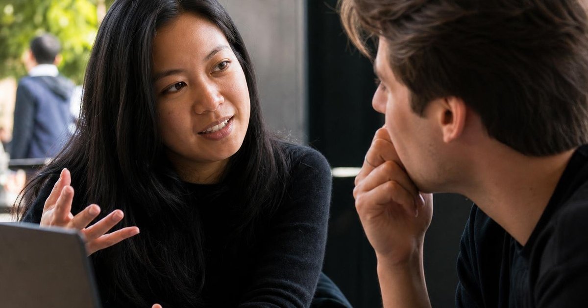 Close-up candid of Melbourne AI meetup attendees discussing laptops and event badges at a tech venue