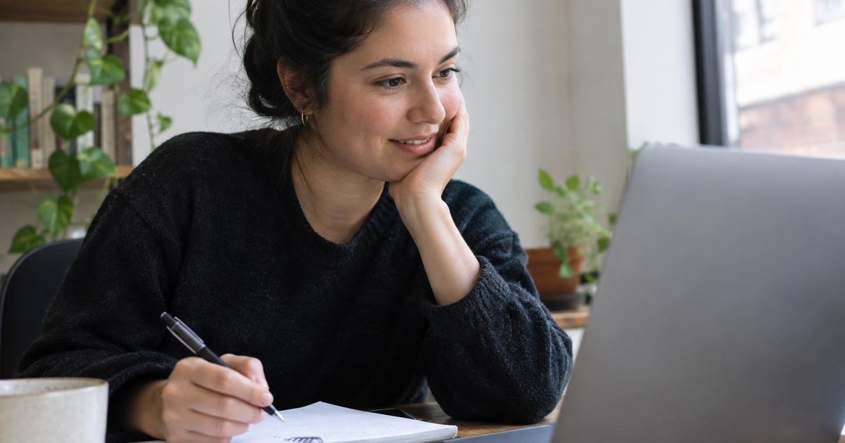 Person writing notes beside an open laptop at a desk