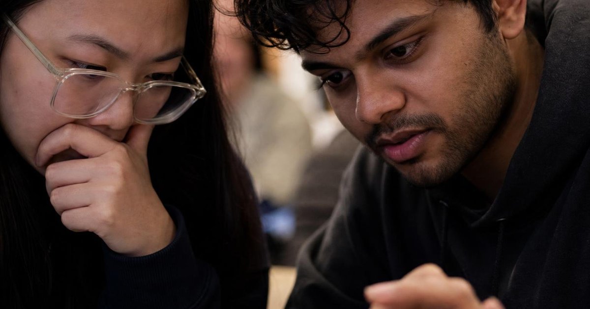 Hands checking Melbourne AI hackathon listings on a laptop at a casual builder meetup