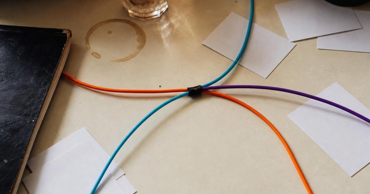Marked-up startup notebooks, coffee cups and tangled cables converging across a shared desk