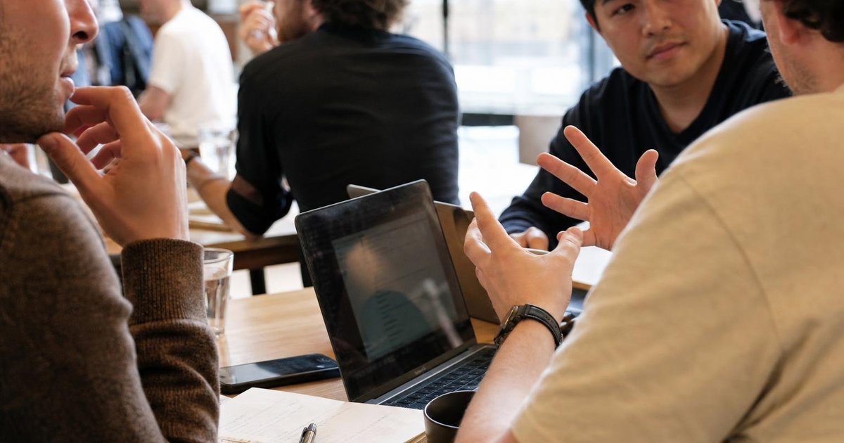 Hands, notebooks and coffee cups around a whiteboard during an Australian AI meetup project discussion