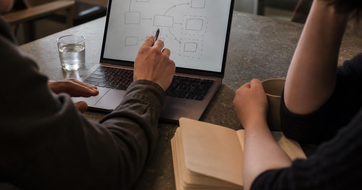AI builder and prospective user sketching a focused workflow prototype on a laptop beside notes and coffee
