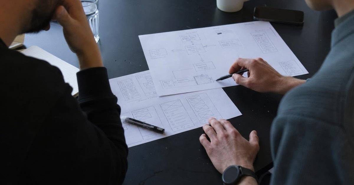 Founder and customer review a workflow sketch and prototype screens over coffee at a shared table