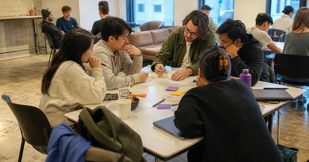 Australian startup meetup in a shared workspace, founders gathered around a product experiment board