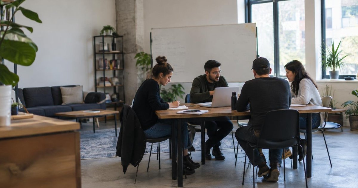 Four people meeting around a table with a laptop and whiteboard