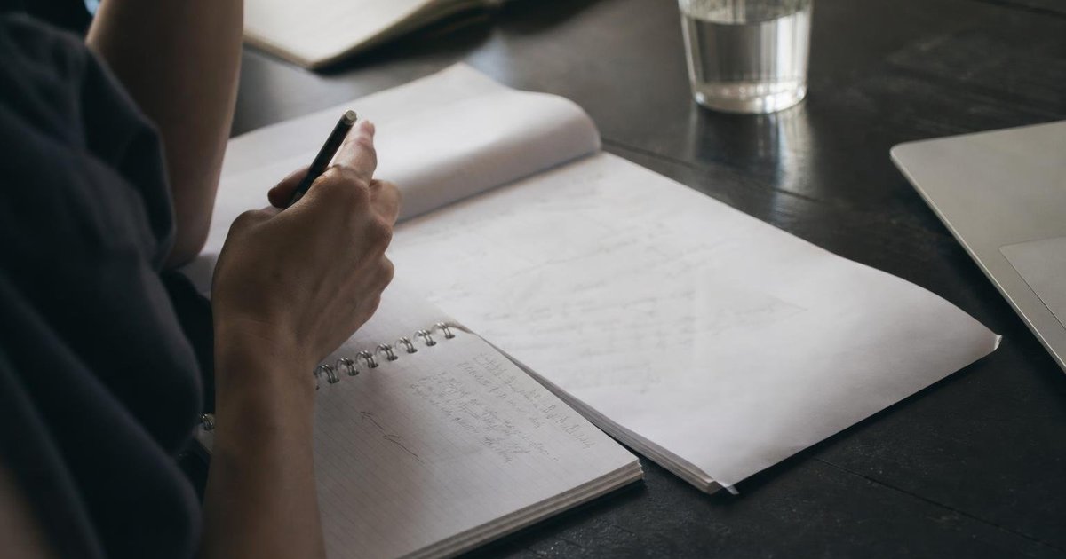 Founder\u2019s handwritten funding milestone notes beside a coffee cup and laptop on a cluttered desk