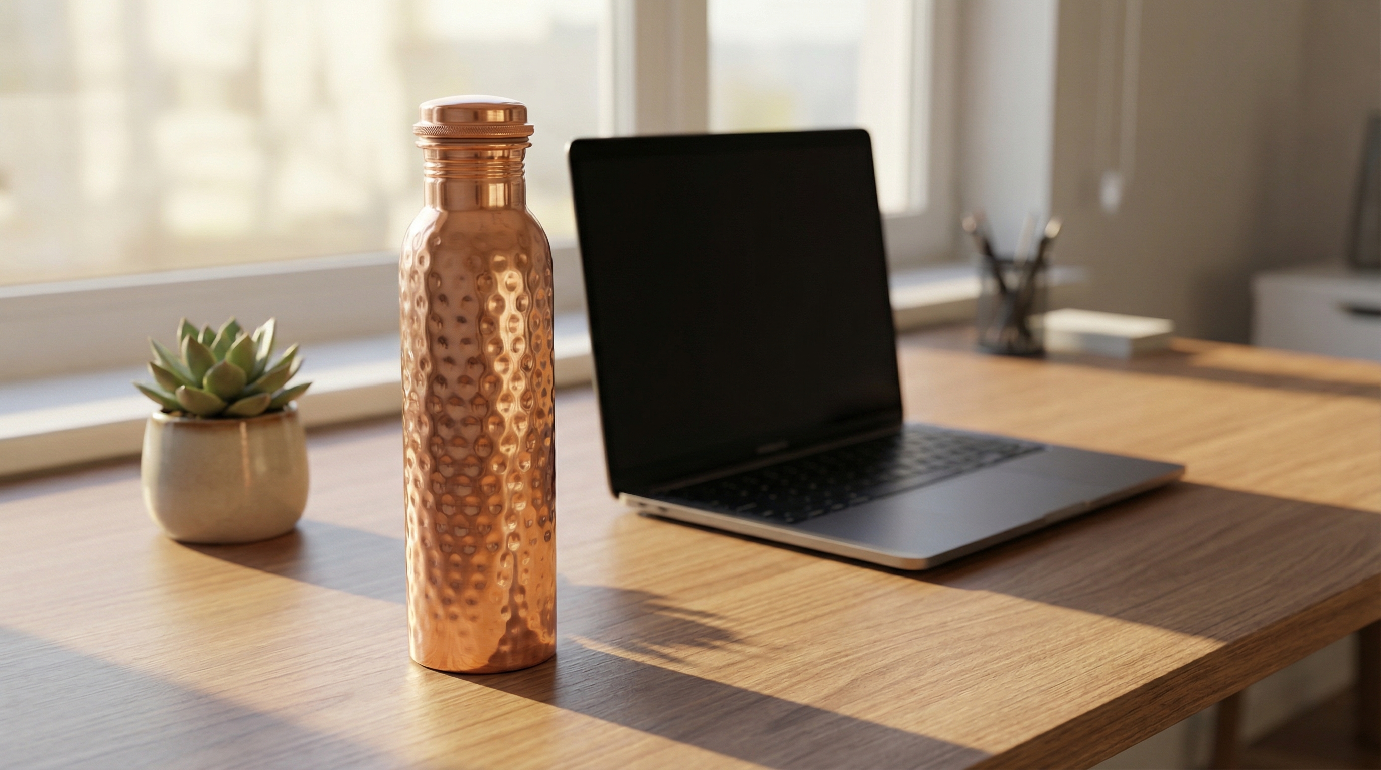 A hammered copper water bottle with a screw-on lid, cylindrical body with a tapered neck, small hammered dents, highly polished rose-gold copper finish sitting on a clean, modern wooden desk next to a laptop and a small succulent plant, soft morning light casting gentle shadows, capturing a quiet moment of everyday hydration, photorealistic, 8k
