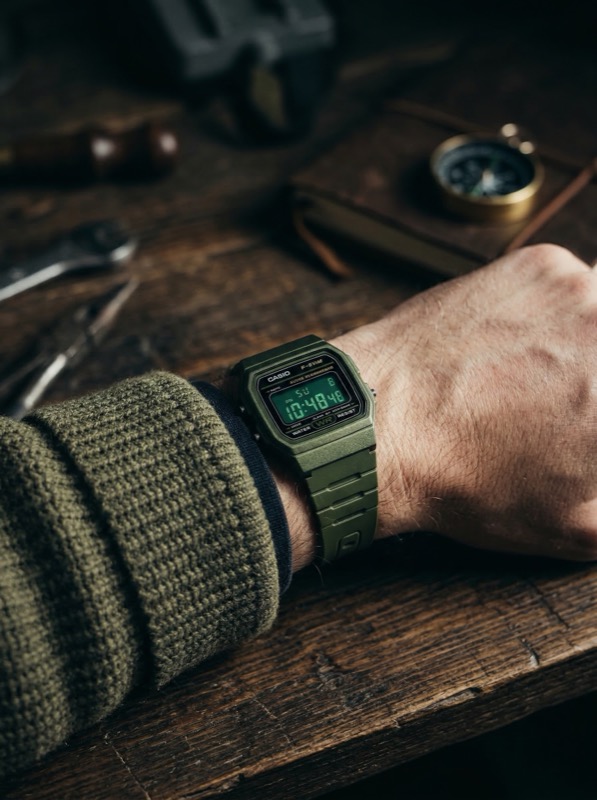 Green digital wristwatch on hand over wooden desk
