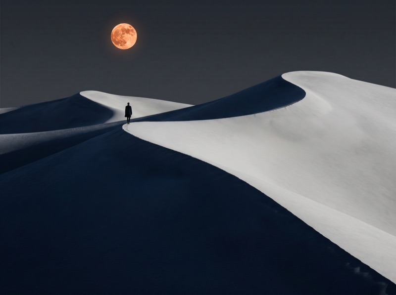 Lone figure on dunes under orange full moon