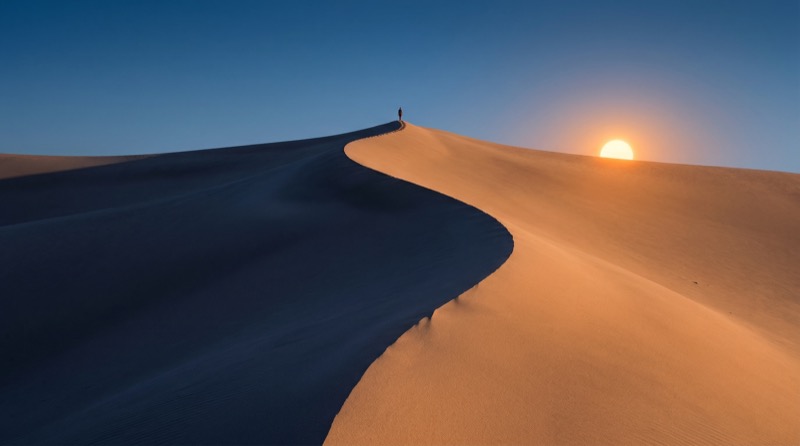 Lone hiker on desert dune at sunset