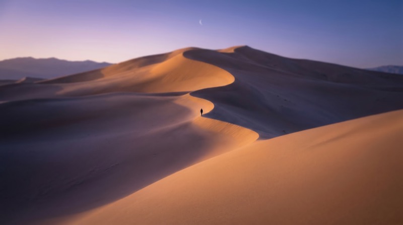 Lone hiker on sunlit desert sand dunes at dusk