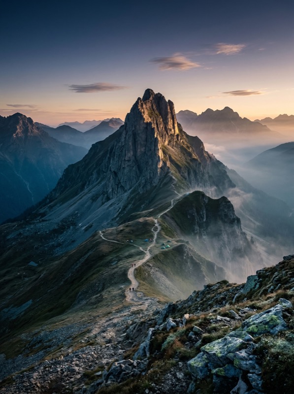 Mountain ridge trail at sunrise with misty valleys