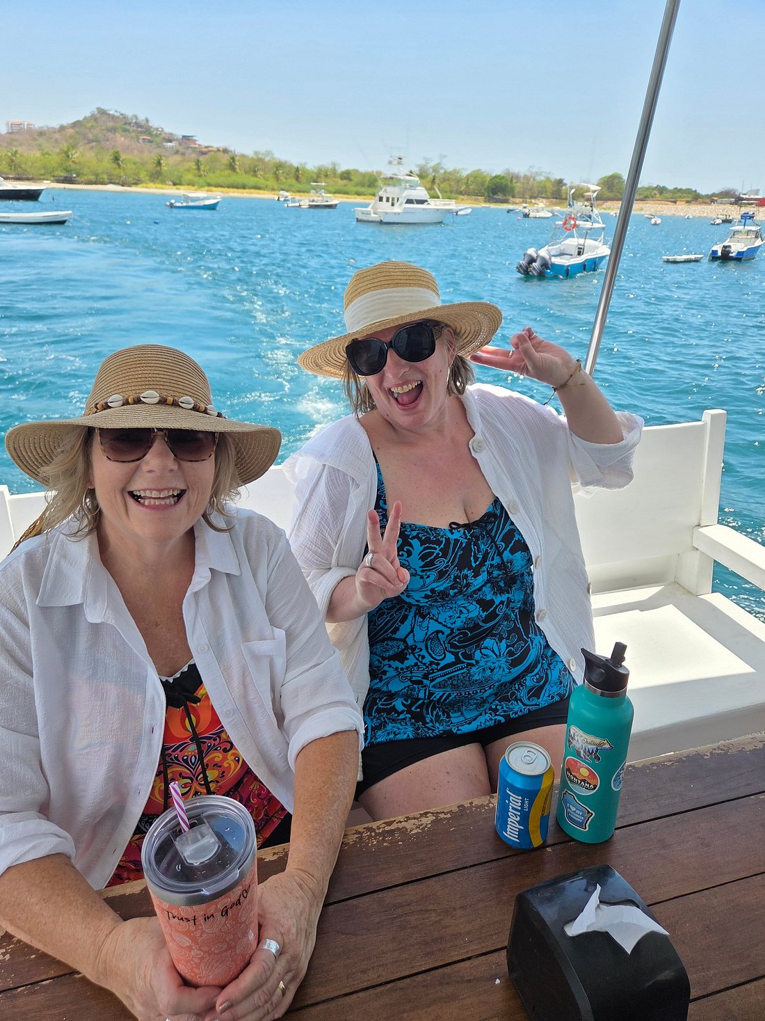 Two guests smiling on board with drinks, marina in the background