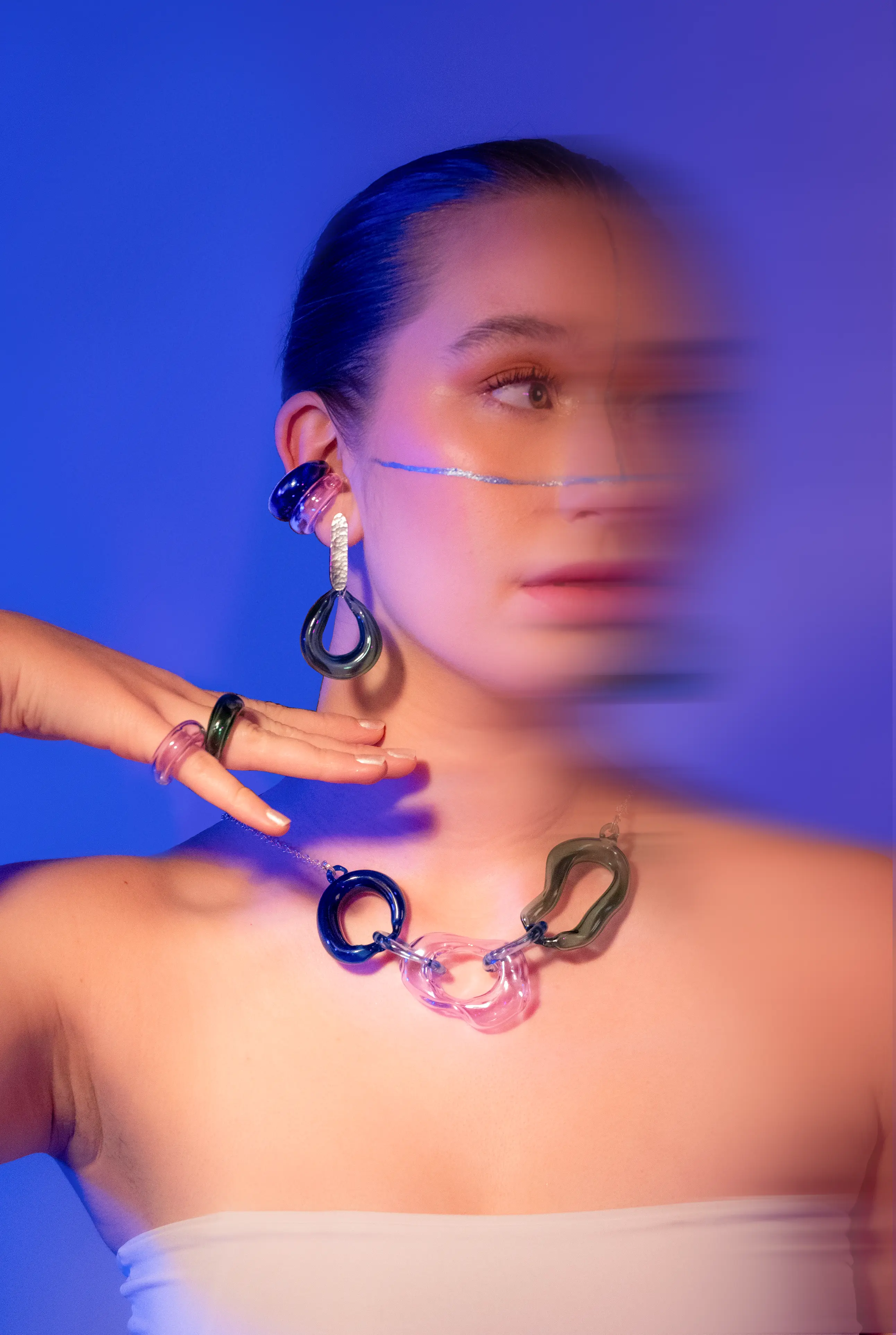 Modelo usando collar, anillo y aretes de vidrio artesanal con estética futurista en tonos azul y rosa.