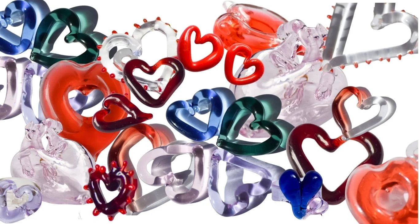 Colección de anillos y ear cuffs de vidrio en forma de corazón dispersos artísticamente, con piezas rojas, azules, verdes, borgoña, transparentes y naranjas en varios diseños escultóricos de corazónRetry
