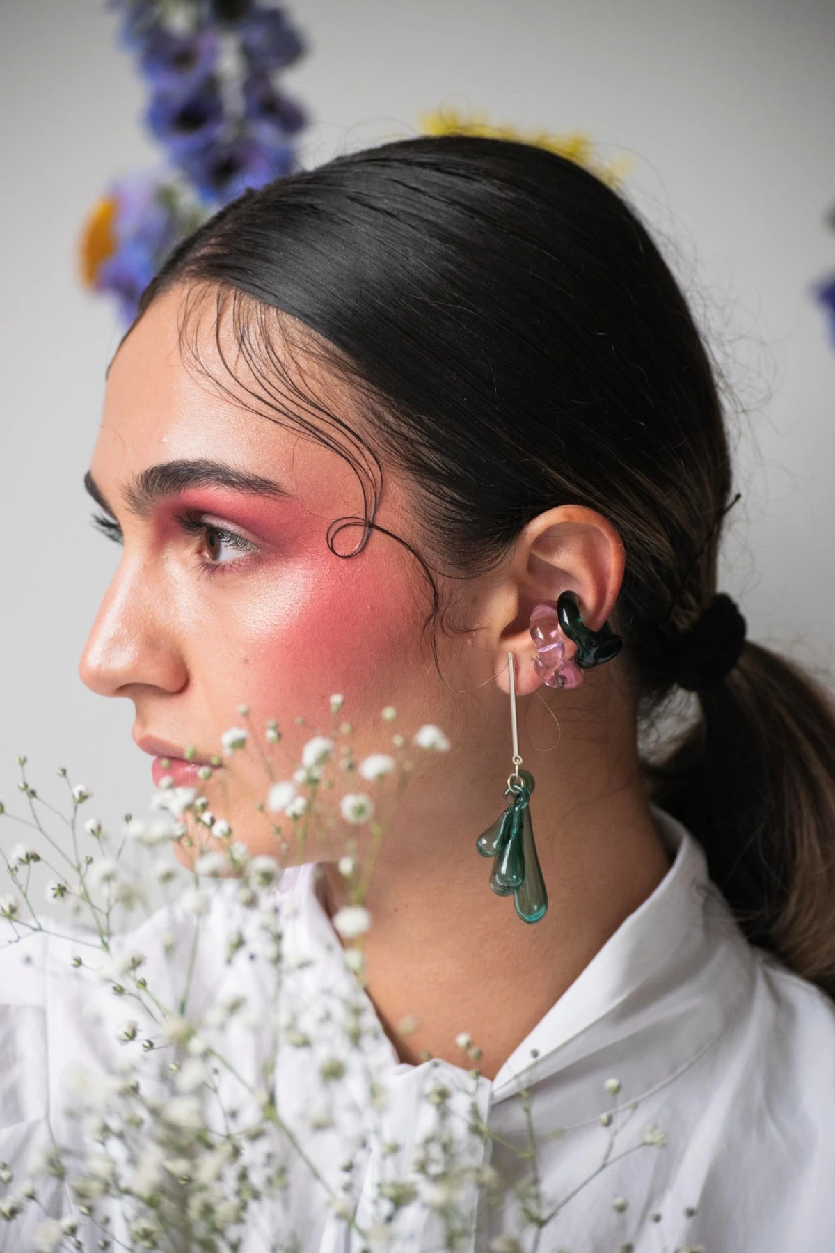 Model wearing green jewelry from our collection looking sideways surrounded by flowers with a timid expression