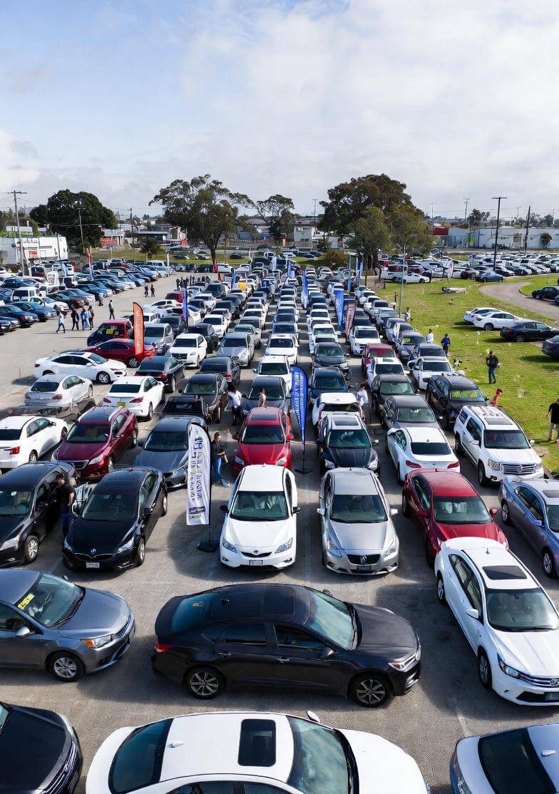 Person performing a VIN check with vinspectorai.com on a laptop in front of used cars at a dealership lot, demonstrating wise used car buying practices in 2026.