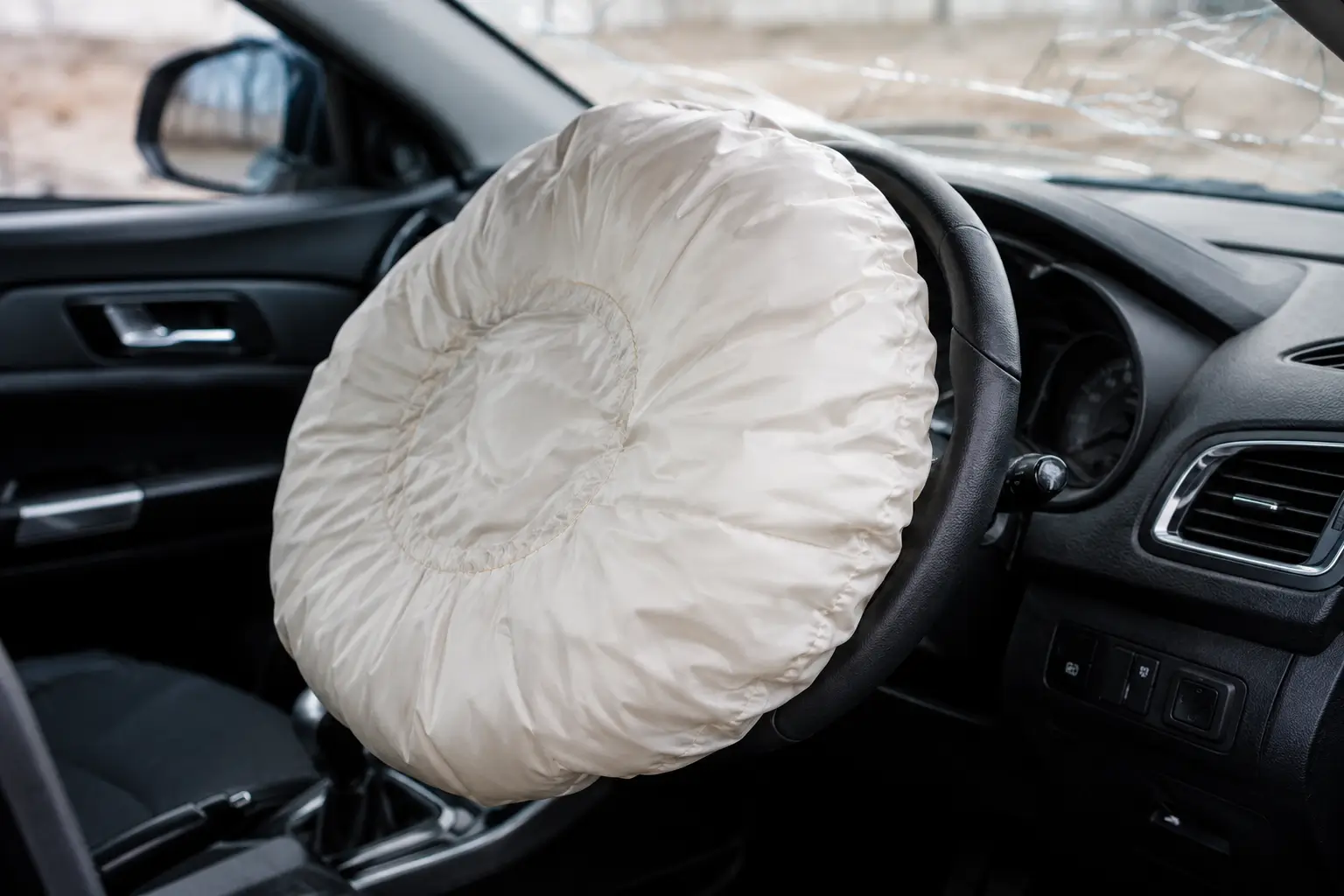 Deployed driver airbag fully inflated from the steering wheel inside a car cabin after a collision, showing what happens when airbags deploy in an accident.