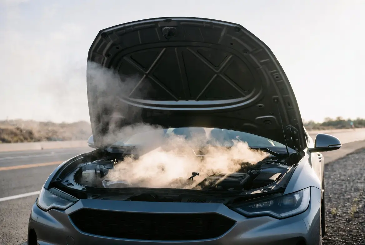 Car with hood open on the side of a road with steam rising from an overheating engine, showing a common car engine problem requiring immediate attention.