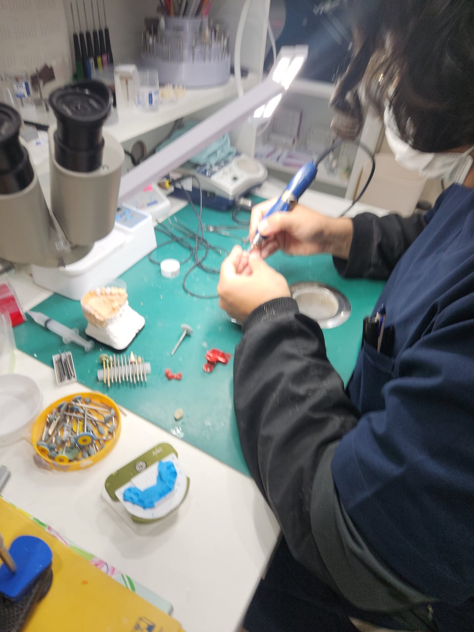 A dental technician working under a magnifier at a workbench