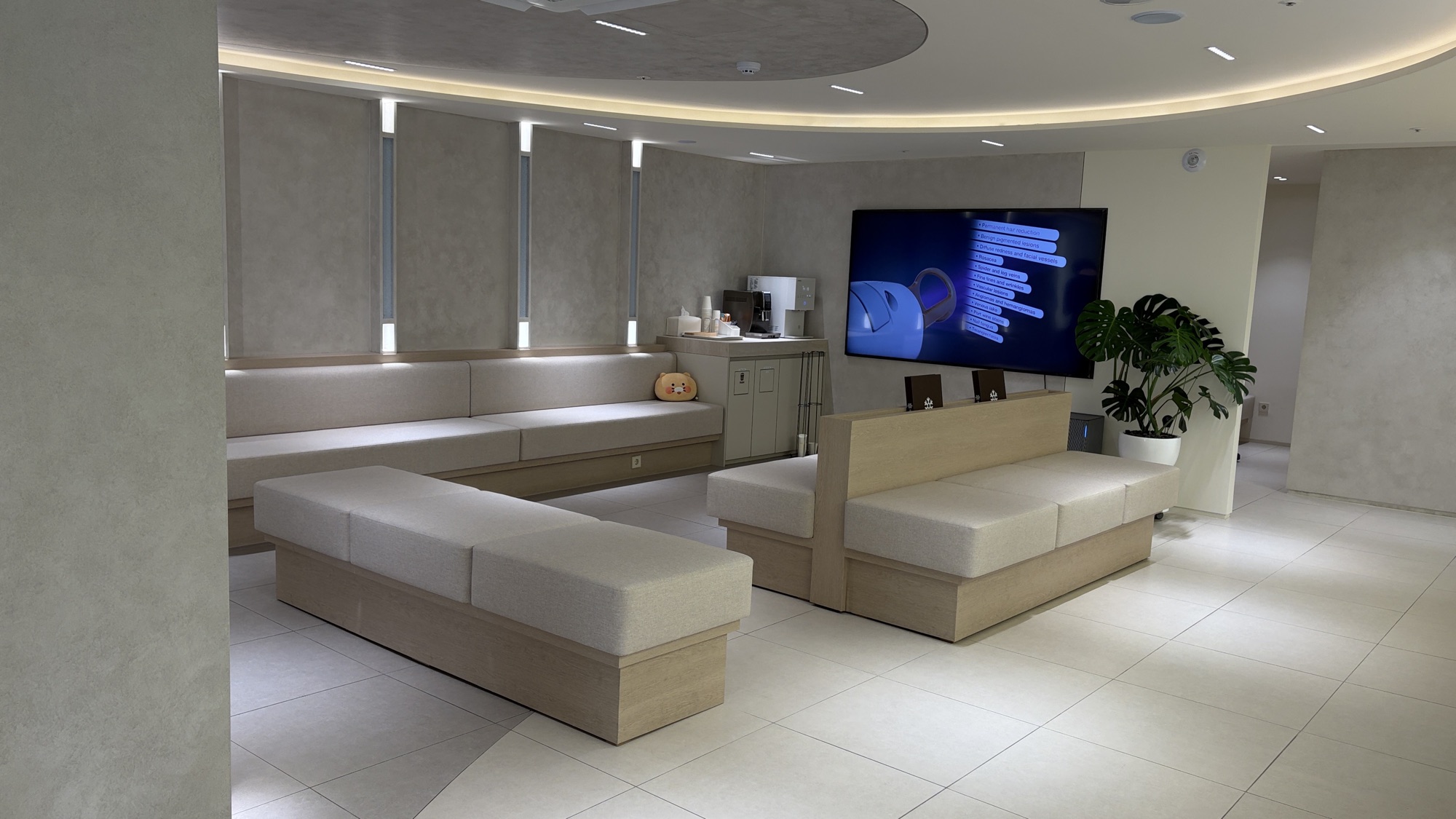 Waiting lounge with long bench seating and a wall-mounted screen