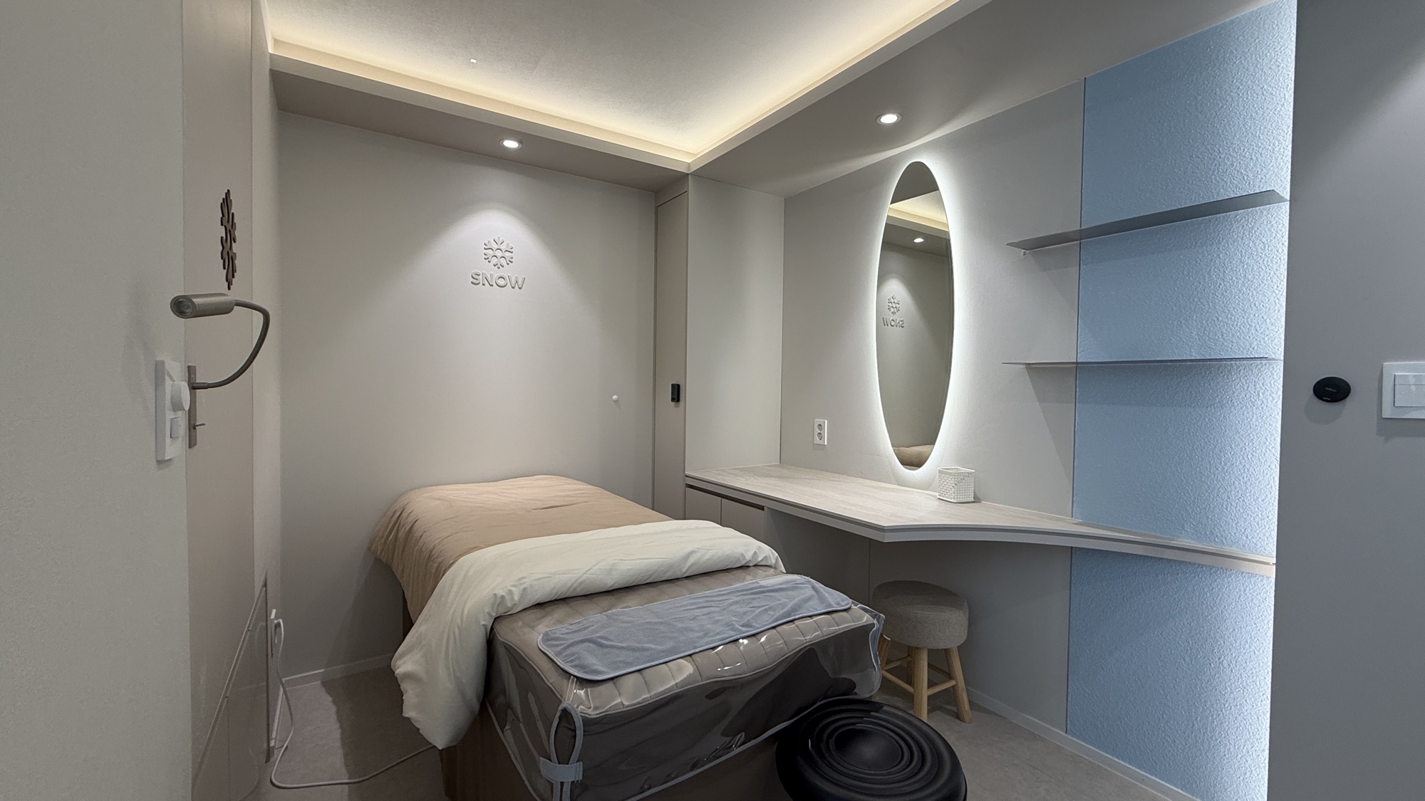Single treatment room with an oval mirror and blue wall shelving