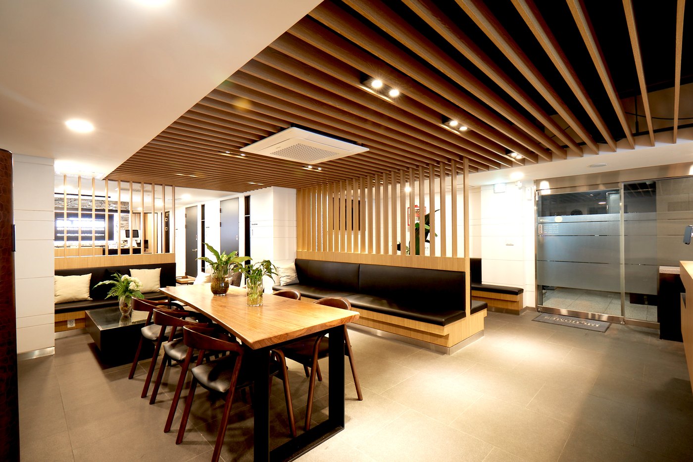 Waiting lounge under a slatted wood ceiling, with a long communal table and bench seating