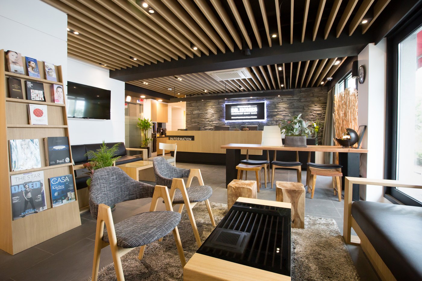 Daylit lounge with armchairs and a magazine rack, facing the information desk against a stone feature wall