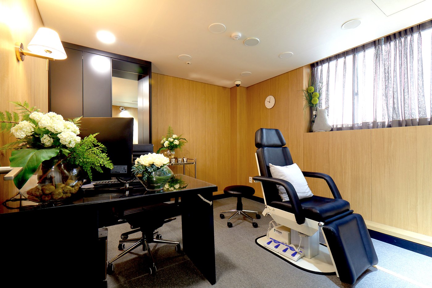 Single treatment room with a reclining chair beside a curtained window