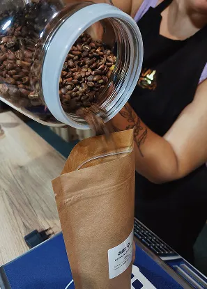Процес наповнення крафтового паперового пакету свіжо обсмаженою кавою