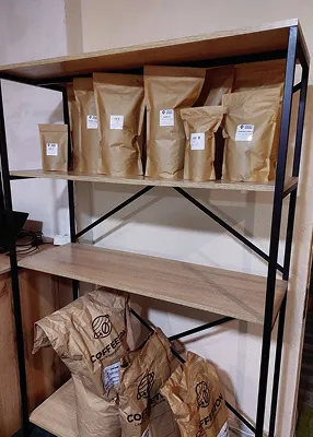 Декоративний стенд: на верхніх поличках розміщені пакети з кавою різної ваги, а внизу — великі мішки з кавою