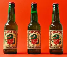 Три скляних пляшки на помаранчевому фоні. На етикетці желений чудік