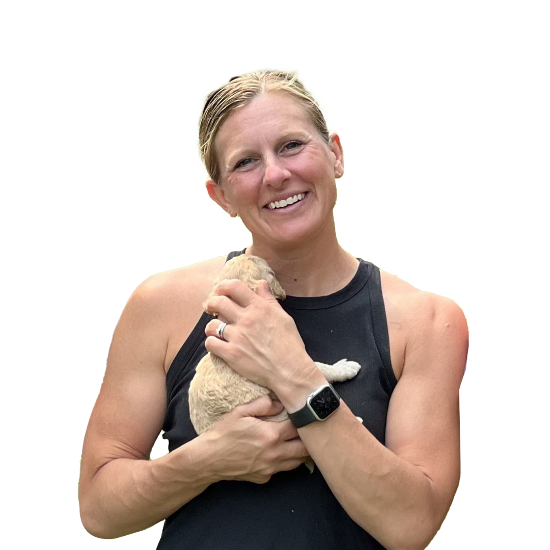 Janelle smiling in a black sleeveless top while holding a small puppy against a soft green background.