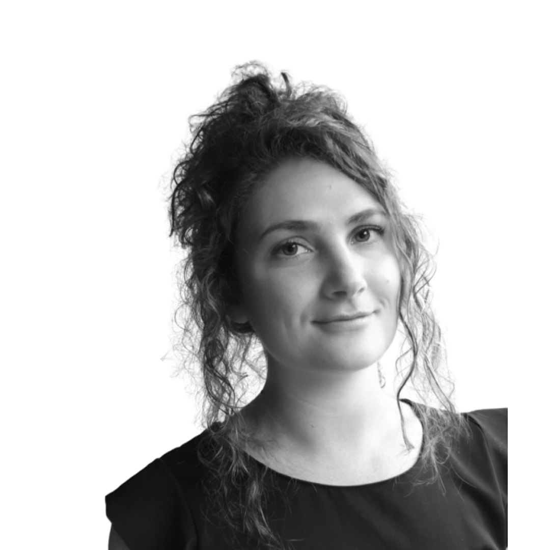 Black-and-white portrait of Jess with curly hair in a loose updo, smiling slightly against a plain white background.