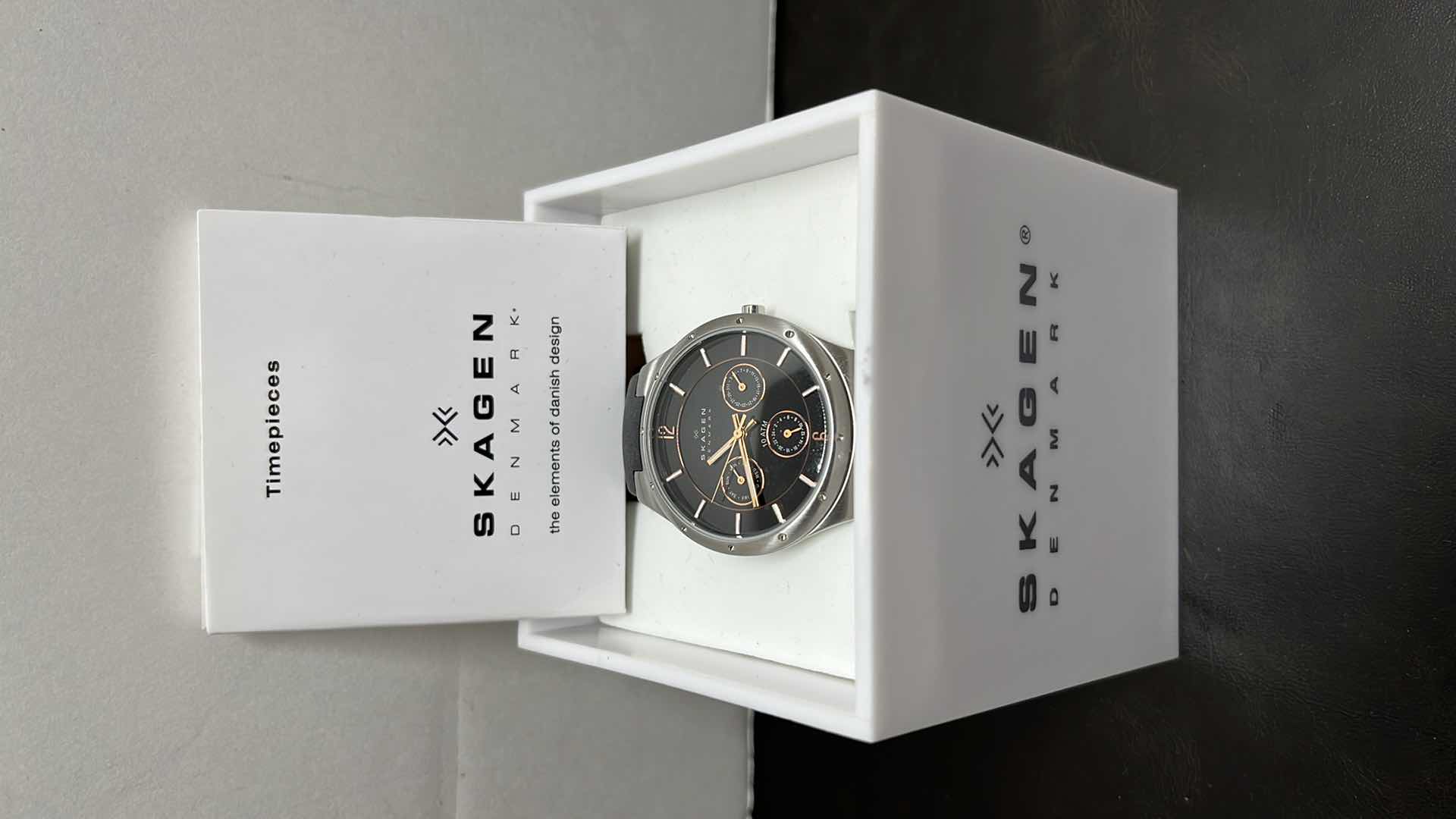 Photo 1 of MENS SKAGEN DENMARK STAINLESS STEEL CASE MULTIFUNCTION WATCH W RUBBER STRAP, BLACK DIAL W ROSE GOLD INDICATORS IN ORIGINAL BOX, MODEL 377LSRBO