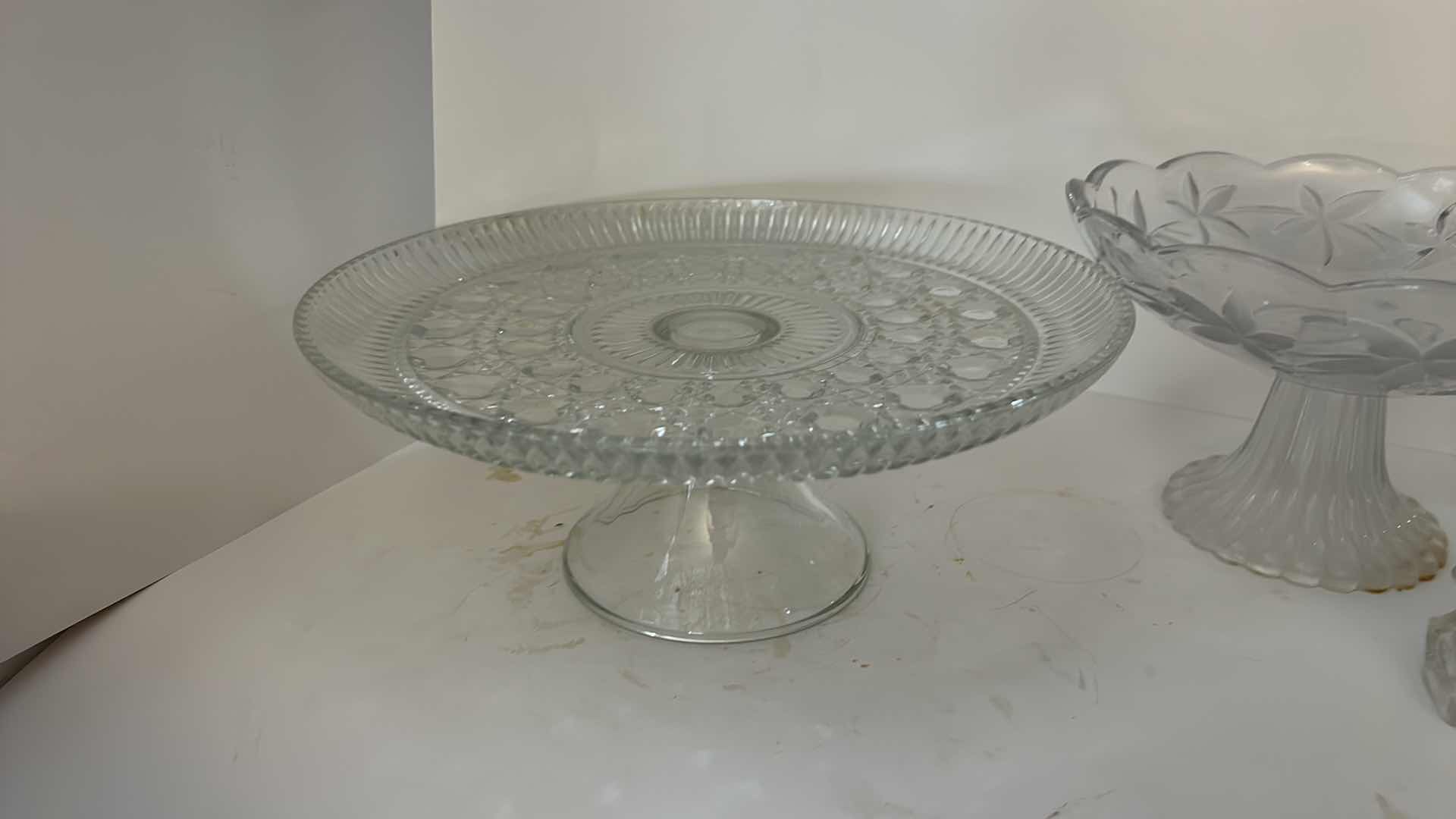 Photo 1 of ASSORTED VINTAGE CLEAR PRESSED GLASS SERVING PIECES INCLUDING DECORATIVE ROUND PLATTER, PEDESTAL COMPOTE AND FLORAL RELIEF DISH.
ESTIMATED RETAIL VALUE: $40–$60 FOR THE GROUP.