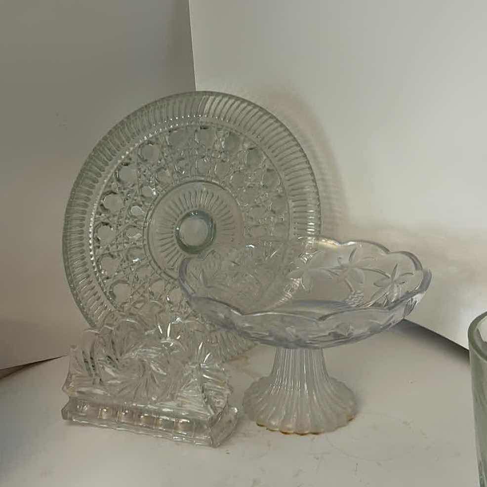 Photo 1 of ASSORTED VINTAGE CLEAR PRESSED GLASS SERVING PIECES INCLUDING DECORATIVE ROUND PLATTER, PEDESTAL COMPOTE AND FLORAL RELIEF DISH.
ESTIMATED RETAIL VALUE: $40–$60 FOR THE GROUP.