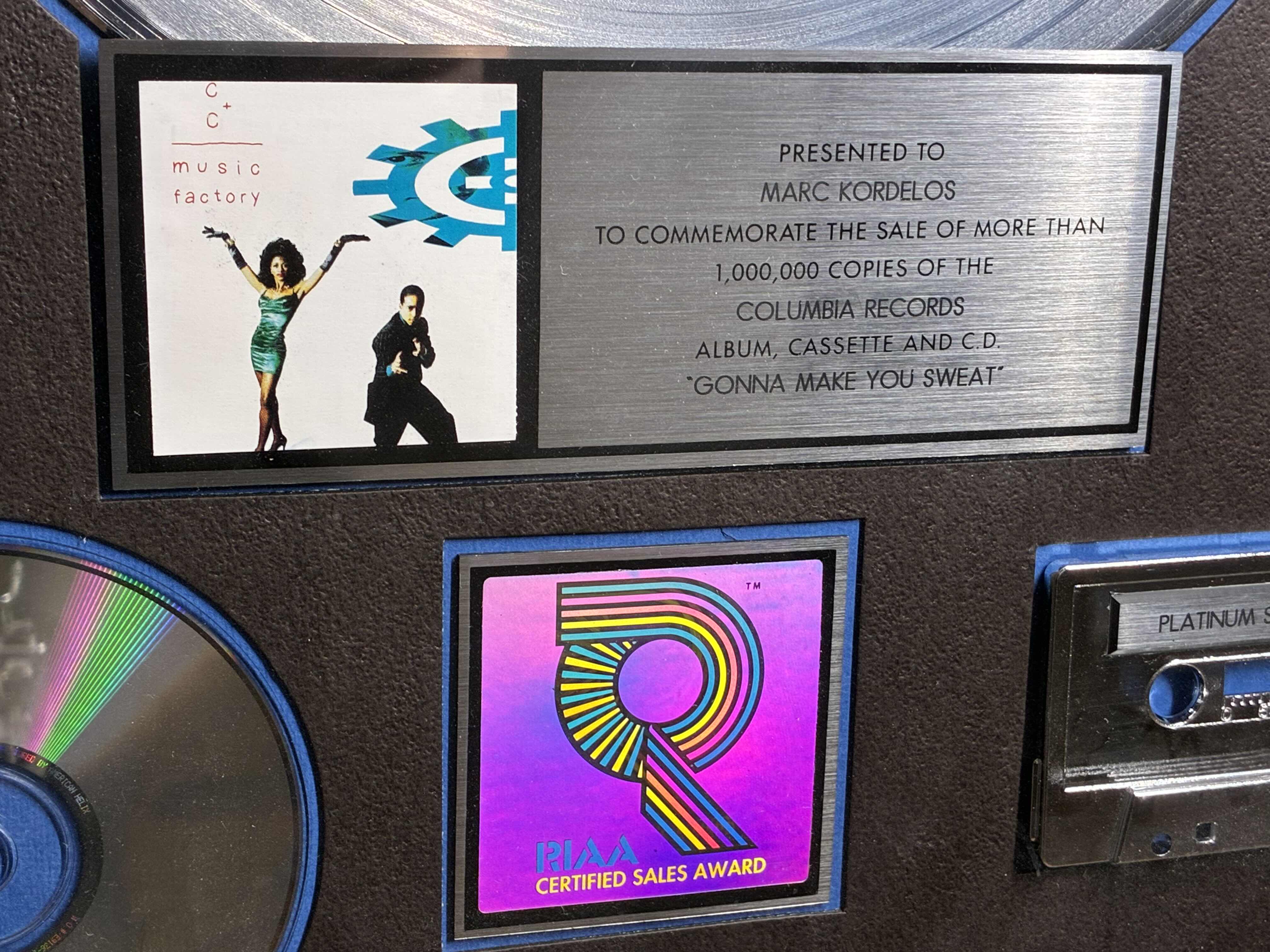 Photo 1 of PLATINUM RECORD PRESENTED TO MARC KORDELOS TO COMMEMORATE THE SALE OF MORE THAN $1M COPIES OF THE COLUMBIA RECORDS ALBUM, CASSETTE & CD
"GONNA MAKE YOU SWEAT" FRAMED PLAQUE 17“ X 21“